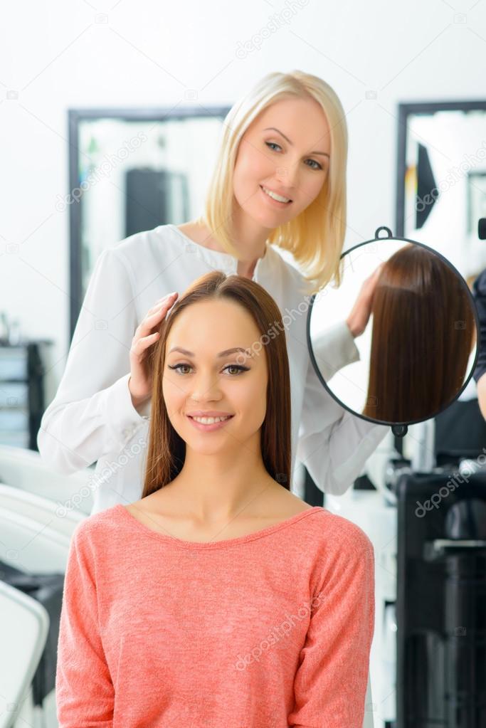 Stylist is showing hairdo to her client.