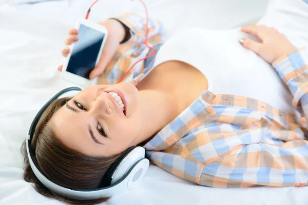 Menina positiva deitada na cama e ouvindo música . — Fotografia de Stock