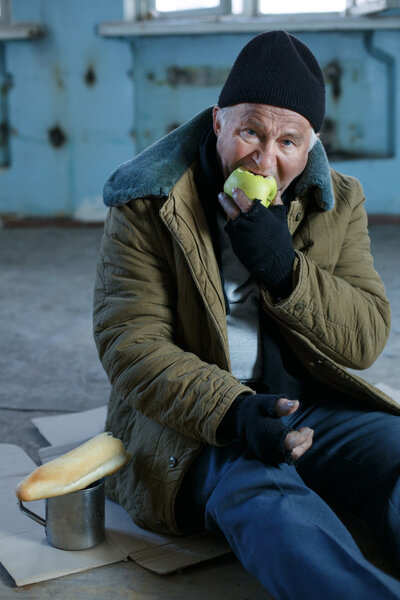 Senior homeless man eating an apple.