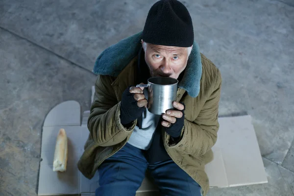 Homeless old man drinking from iron mug. — Stock Photo, Image