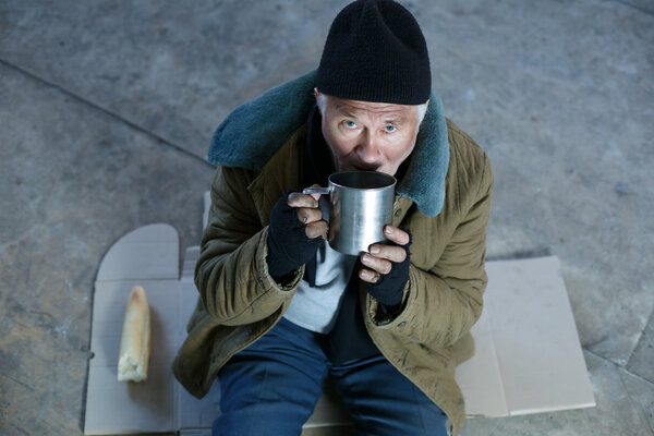 Homeless old man drinking from iron mug.