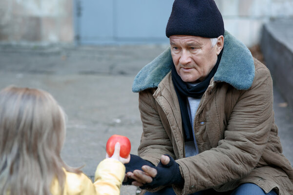 Little girl gives apple to the beggar.