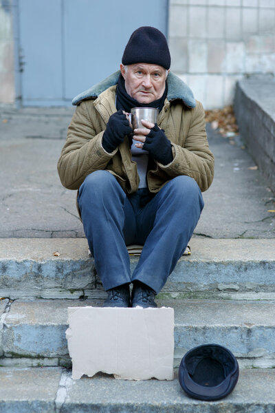 Homeless man holding his iron cup.