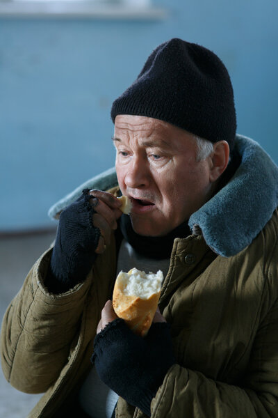 Depressed senior-aged beggar eating bread.