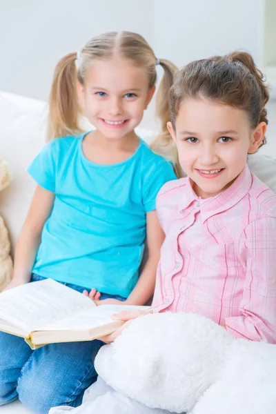 Cheerful little sisters sitting on the sofa — ストック写真