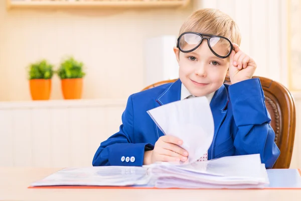 Little boy is smiling while sitting at the desk. — Stock Photo, Image