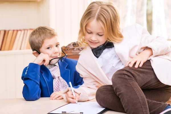 Menina assinando papéis e menino sentado na mesa . — Fotografia de Stock