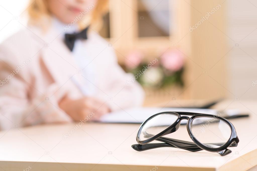 Eyeglasses are resting on surface of the desk.