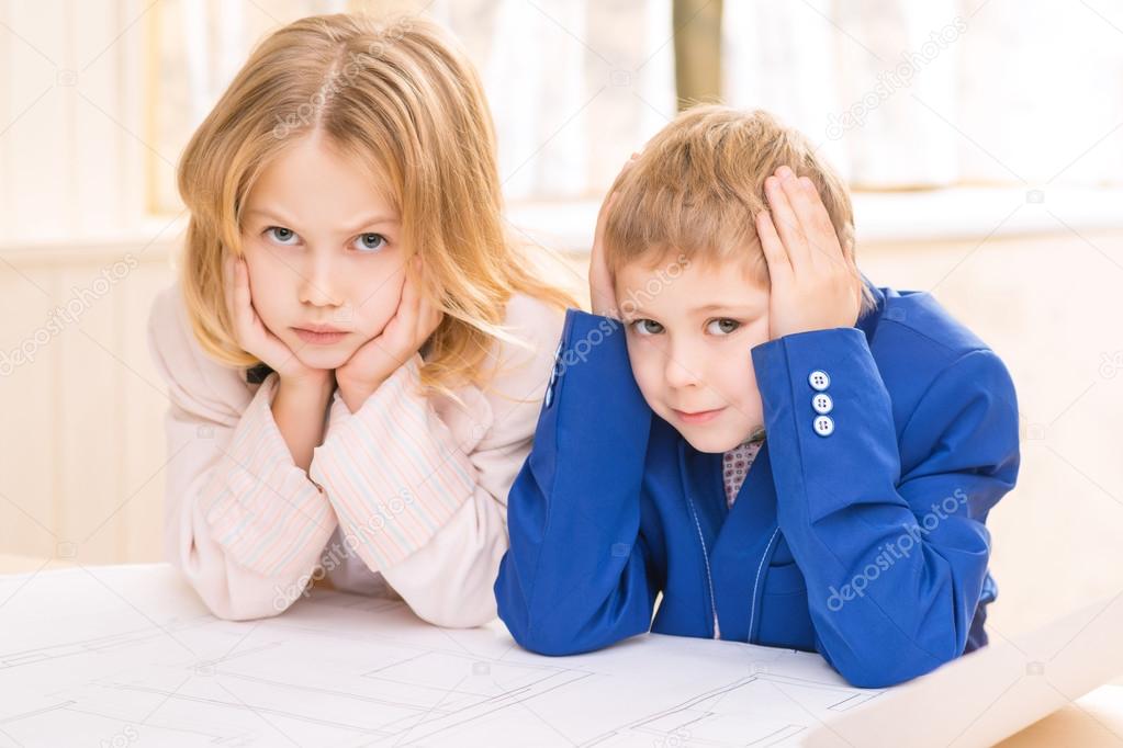 Small kids are leaning on table and frowning.