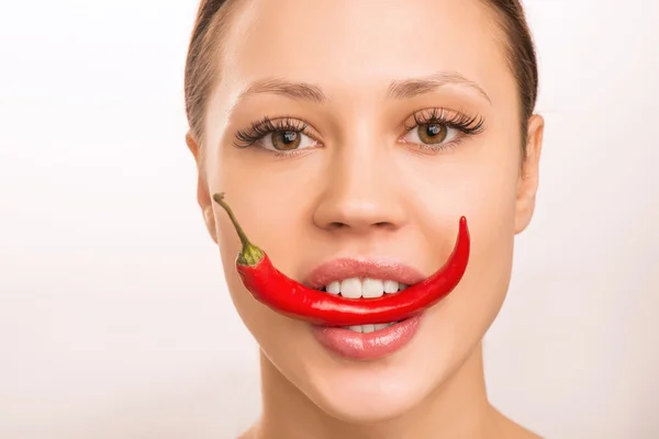 Jovem está segurando pimenta vermelha com os dentes . — Fotografia de Stock