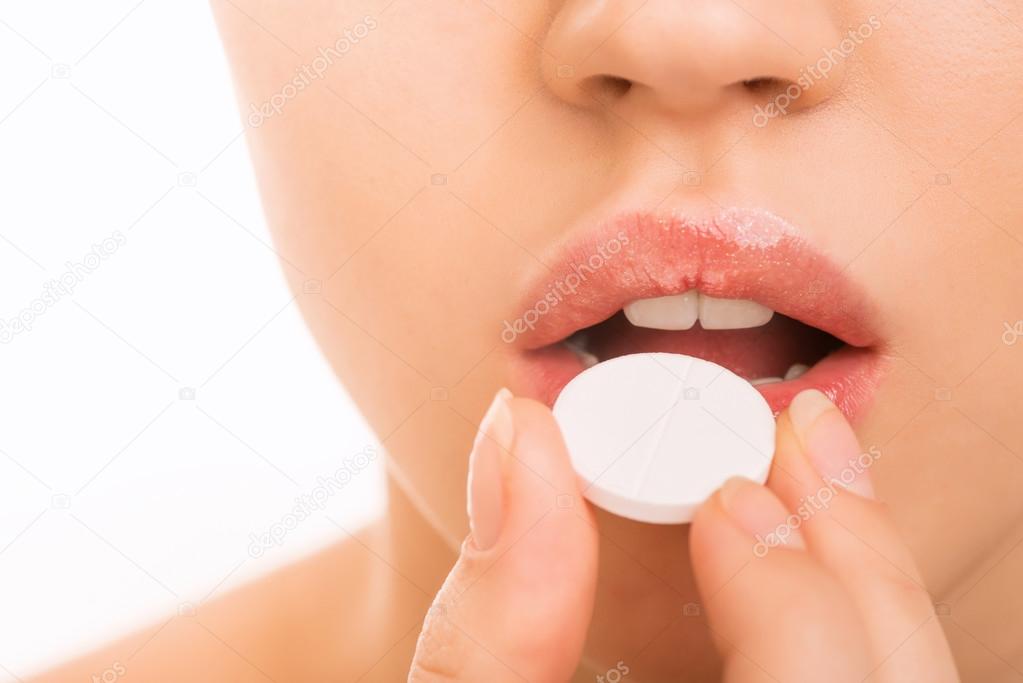 Young girl bringing a pill to her mouth.