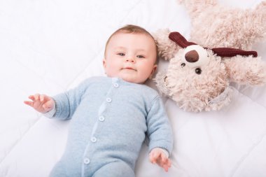 Küçük yürümeye başlayan çocuk onun oyuncak ile yatakta yatıyor.