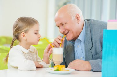 granddaughter  enjoying a drink with grandfather.