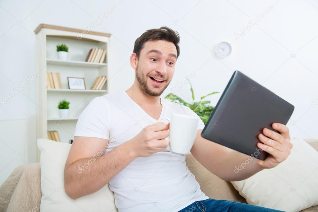 Young surprised man with cup and tablet.