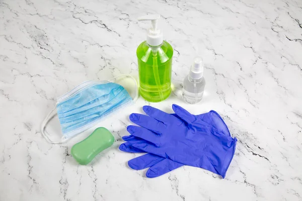 Medical mask, blue gloves, green soap, bottles of green liquid on a white marble background. Medicine viral infection covid-19 pandemic vaccines remedies.