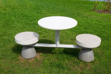 Yuvarlak bir masa ve açık güneşli bir günde açık yeşil arka planda gri renkli tek bir metal yapıda yapılmış iki yüksek sandalye. Eğlence parkı mimarisi.