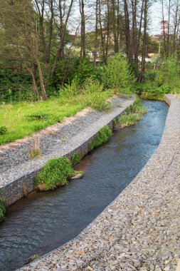 Nehir akıntısı için granit taşlardan yapılmış bir kanal. Üzerinde çimenler ve çalılar var. Şehrin peyzajı, nehir hidrolojisi..
