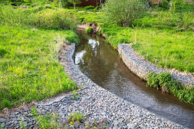 Nehir akıntısı için granit taşlardan yapılmış bir kanal. Üzerinde çimenler ve çalılar var. Şehrin peyzajı, nehir hidrolojisi..