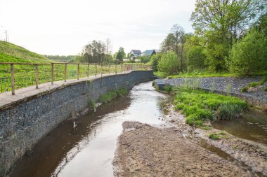Nehir akıntısı için granit taşlardan yapılmış bir kanal. Üzerinde çimenler ve çalılar var. Şehrin peyzajı, nehir hidrolojisi..