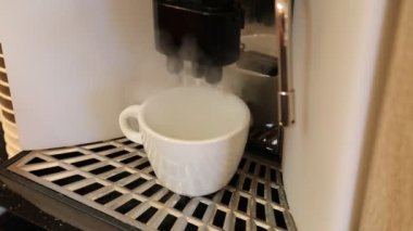 Kahve makinesindeki beyaz bir fincana sıcak süt ve kahve dökülüyor. Teknolojiler kamu hizmeti işi.