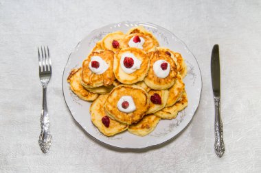 Ekşi kremalı turuncu cheesecake yuvarlak tabakta çilek, çatal ve bıçak. Şekerleme ürünleri çay içerler..