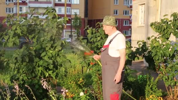 Ogrodnik Kombinezonie Żółtym Wężem Podlewa Kwiaty Krzewy Tle Budynków Mieszkalnych — Wideo stockowe