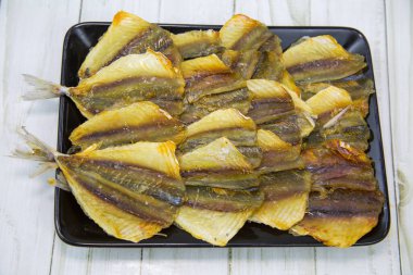 Sarı tekir (Latince: Selaroides leptolepis) siyah dikdörtgen bir plaka üzerinde ahşap bir masa arkaplanıyla sıralanmış olarak kurutulmuştur. Yiyecek bira için lezzetli bir atıştırmalıktır..