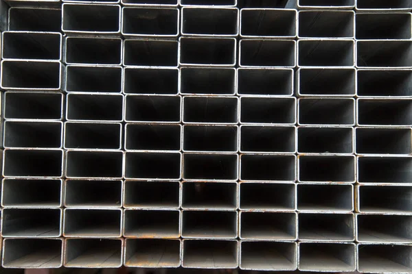 ラックに積み込まれた錆の痕跡を持つ長方形の金属パイプの端からの眺め 建設生産の背景 — ストック写真