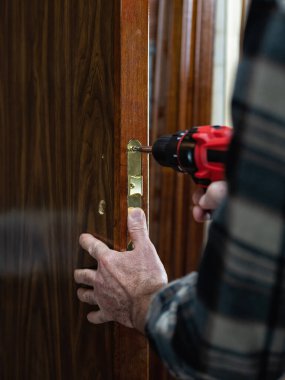 Yakın plan. Elektrikli tornavidayla marangoz ahşap bir kapının kilidini tamir ediyor. İnşaat endüstrisi. 