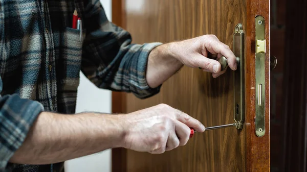 Yakın plan. Marangoz tornavidayla ahşap bir kapının kilidini tamir ediyor. İnşaat endüstrisi. 
