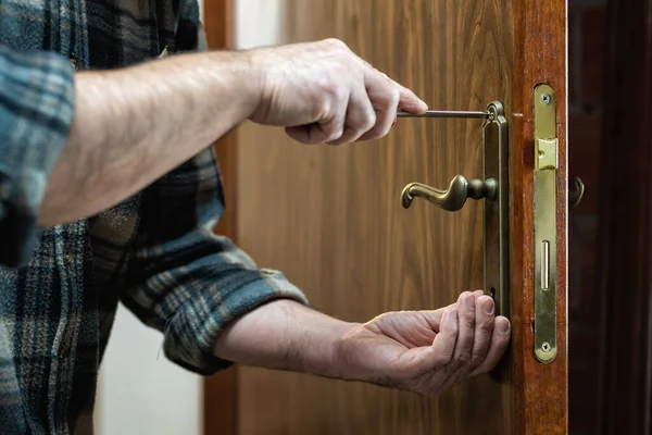 Yakın plan. Marangoz tornavidayla ahşap bir kapının kilidini tamir ediyor. İnşaat endüstrisi. 