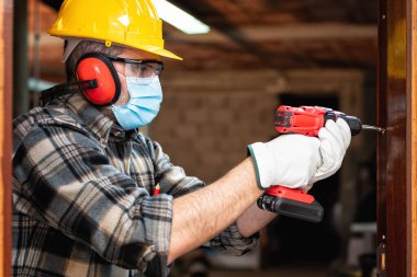 Marangoz, Coronavirus enfeksiyonunu önlemek için bir oda kapısını tamir eder ve takar. İş yerinde Covid-19 salgınını önlemek. Marangozluk.
