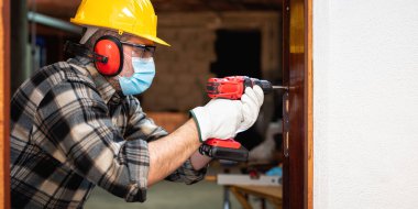 Marangoz, Coronavirus enfeksiyonunu önlemek için bir oda kapısını tamir eder ve takar. İş yerinde Covid-19 salgınını önlemek. Marangozluk.