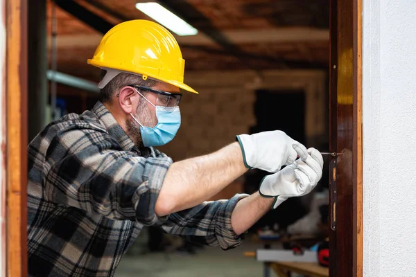 Carpenter worker at work repairs and installs a room door, wear the surgical mask to prevent Coronavirus infection. Preventing Pandemic Covid-19 at the workplace. Carpentry.