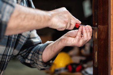 Yakın plan. Marangoz tornavidayla ahşap bir kapının kilidi için plaketi tamir ediyor. İnşaat endüstrisi. 