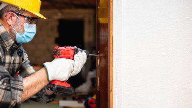 Marangoz, Coronavirus enfeksiyonunu önlemek için bir oda kapısını tamir eder ve takar. İş yerinde Covid-19 salgınını önlemek. Marangozluk. Metin uzayı.