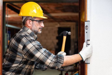 Carpenter worker at work with screwdriver, repairs and installs the door frame of a room. Construction industry. Carpentry. clipart