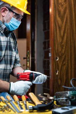 Marangoz, Coronavirus enfeksiyonunu önlemek için bir oda kapısı kilidi takıp cerrahi maske takıyor. İş yerinde Covid-19 salgınını önlemek. Marangozluk.