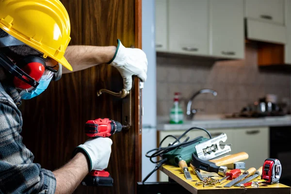 Carpenter worker at work repair and install a room door lock, wear the surgical mask to prevent Coronavirus infection. Preventing Pandemic Covid-19 at the workplace. Carpentry.