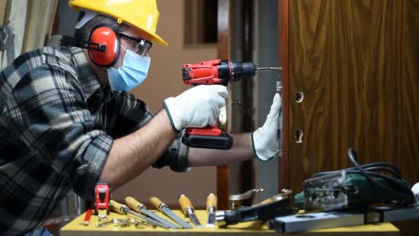 作業修理で大工の労働者と部屋のドアロックをインストールし コロナウイルス感染を防ぐために外科用マスクを着用してください 職場でのパンデミックコビト 19の防止 大工さん — ストック動画