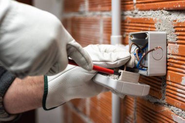 İşteki elektrik işçisi tornavidayla elektrik tesisatının prizlerini tamir ediyor. İnşaat endüstrisi. 