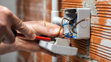 Bir tornavidayla çalışan elektrik işçisi konut elektrik sisteminin anahtarının ucundaki kabloyu tamir ediyor. İnşaat endüstrisi. 