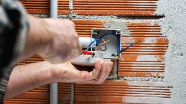 Bir tornavidayla çalışan elektrik işçisi konut elektrik sisteminin anahtarının ucundaki kabloyu tamir ediyor. İnşaat endüstrisi. 