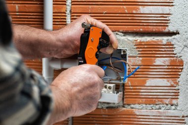 Elektrik işçisi tel sökücüyle birlikte çalışıyor. Konut elektrik sisteminin elektrik kablolarını hazırlıyor. İnşaat endüstrisi. 