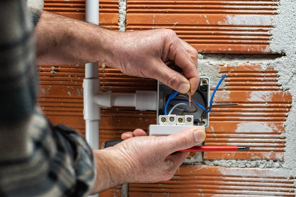 Electrician worker at work inserts the electrical cable into the clamp of a circuit breaker of a residential electrical system. Construction industry.