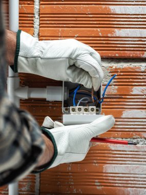 İşteki elektrik işçisi elektrik kablosunu konut elektrik sisteminin devre kesicisine yerleştiriyor. Koruyucu eldivenlerle güvenli bir şekilde çalışmak. İnşaat endüstrisi.