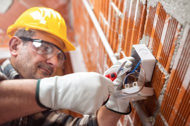 Elektrik işçisi makasla bir elektrik sisteminin elektrik kablolarını hazırlar; kask, eldiven ve gözlük takar. İşyeri güvenliği. 
