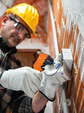 Elektrik işçisi tel sökücü ile elektrik kabloları hazırlıyor; kask, eldiven ve gözlük takıyor. İşyeri güvenliği. 