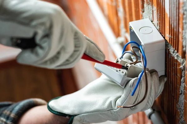 Bottom view. Electrician worker with a screwdriver fixes the cable in the terminal of the switch of an electrical system. Working safely with protective gloves. Construction industry.