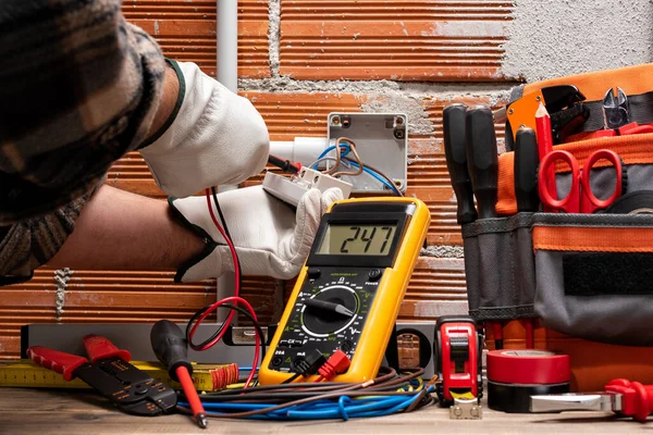 Electrician worker at work with the tester measures the voltage in an electrical system. Working safely with protective gloves. Construction industry.